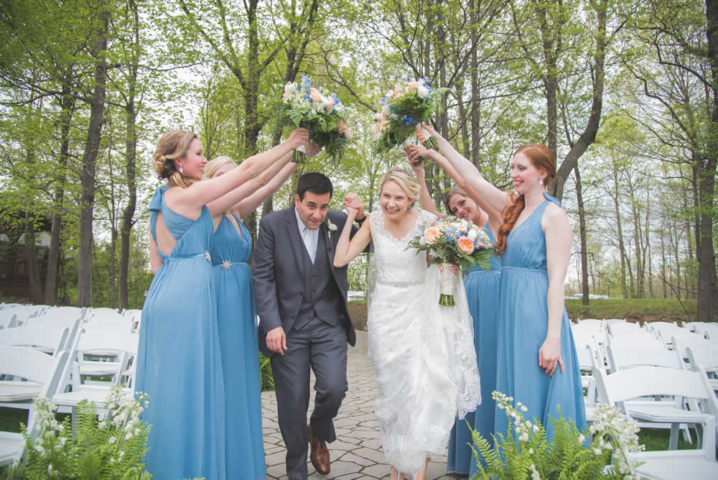 Wedding couple running under a bridge of bride's maid arms