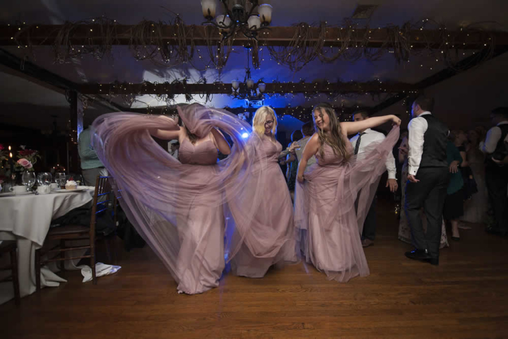 wedding event Women in purple wedding attire are dancing at a reception. They are moving their dresses to create shapes.