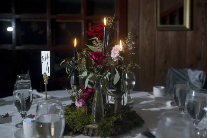 decor Red and pink roses in single vases with black lit candles at the center of a table dressed in white linen. A sign reads table 4.