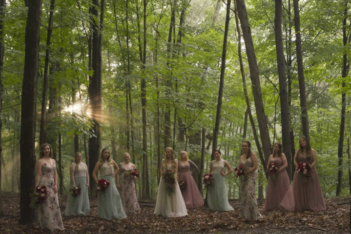 wedding event Ten women in pink, green and white dresses stand outside. The bride is center and everyone holds bouquets.