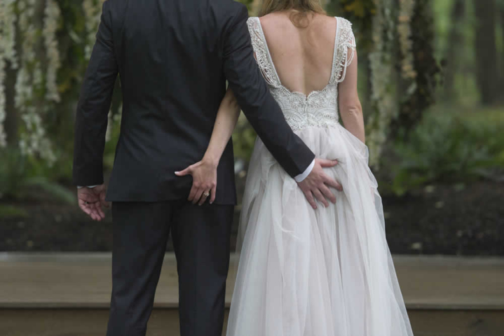 wedding event A couple in wedding attire seen from behind. They each have one hand on each other's bottom.