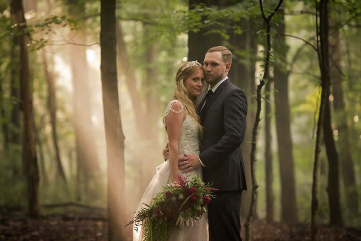 wedding event A couple in wedding attire stand in the forest facing each other looking at the camera