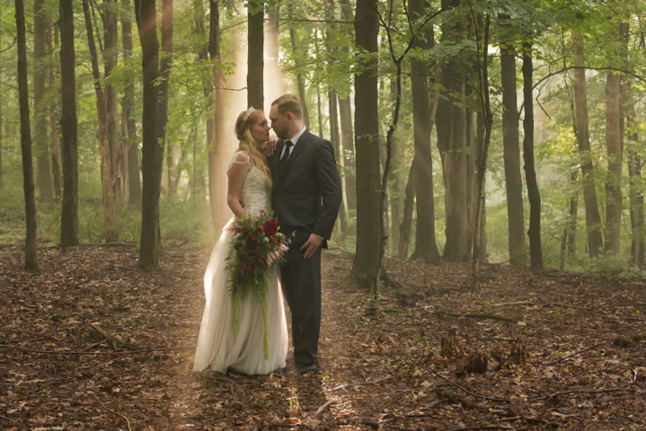 wedding event A couple in wedding attire stand in the forest facing each other.