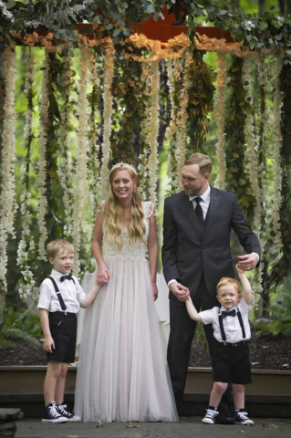 wedding event Bride and groom with two little boys under pavilion with flower vines hanging in the background