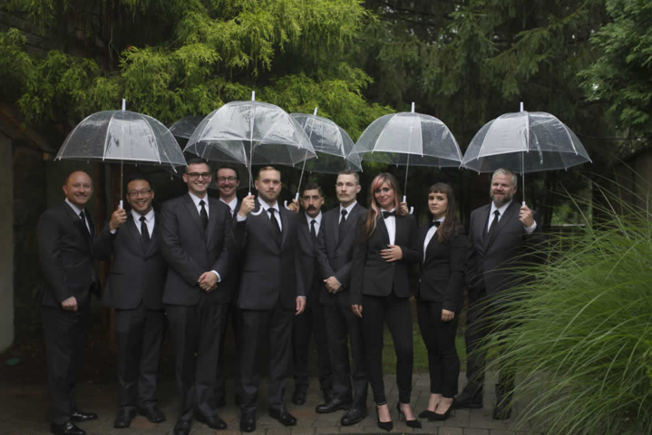 wedding event Groom and wedding co-ed wedding party all in suits, holding umbrellas outside