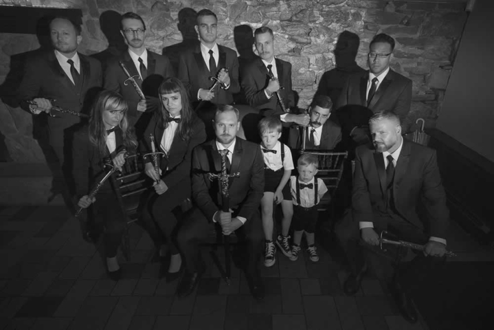 wedding event Black and white photo of groom and co-ed wedding party all in suits. Some are sitting, others stand. They each hold a long sword.