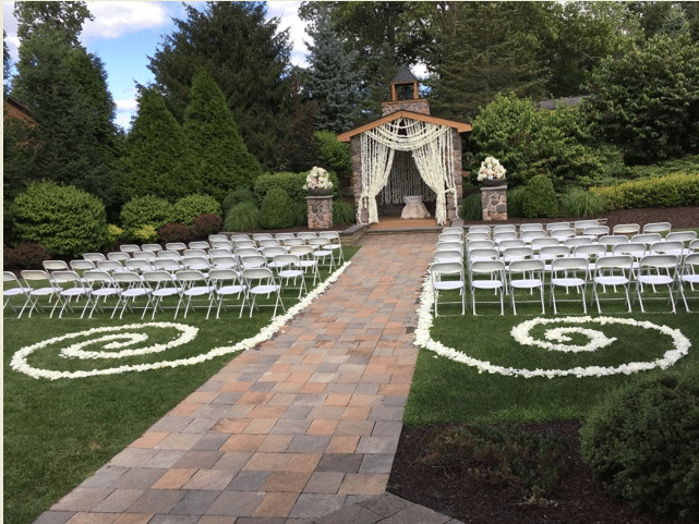 Outdoor altar with white chairs on the lawn with flower petals adorning the grass