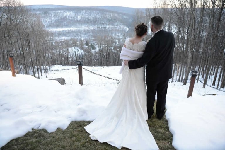 Back of a bride and groom standing at the cliffs looking out over a winter mountain scene