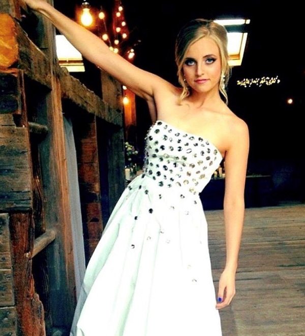 A bride wearing studded wedding gown leans from a wooden structure