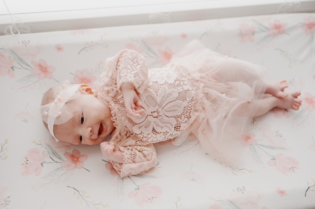Infant girl wearing lace lies on floral mat