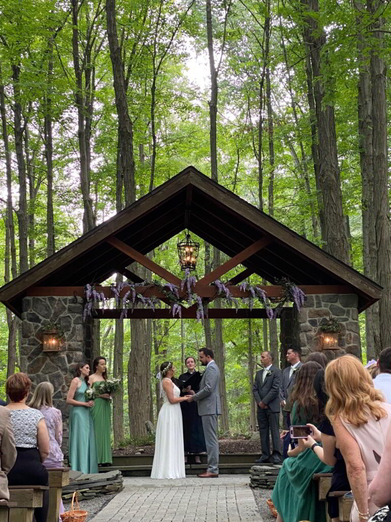 Wedding couple holding hands under a gazebo in the woods - getting married