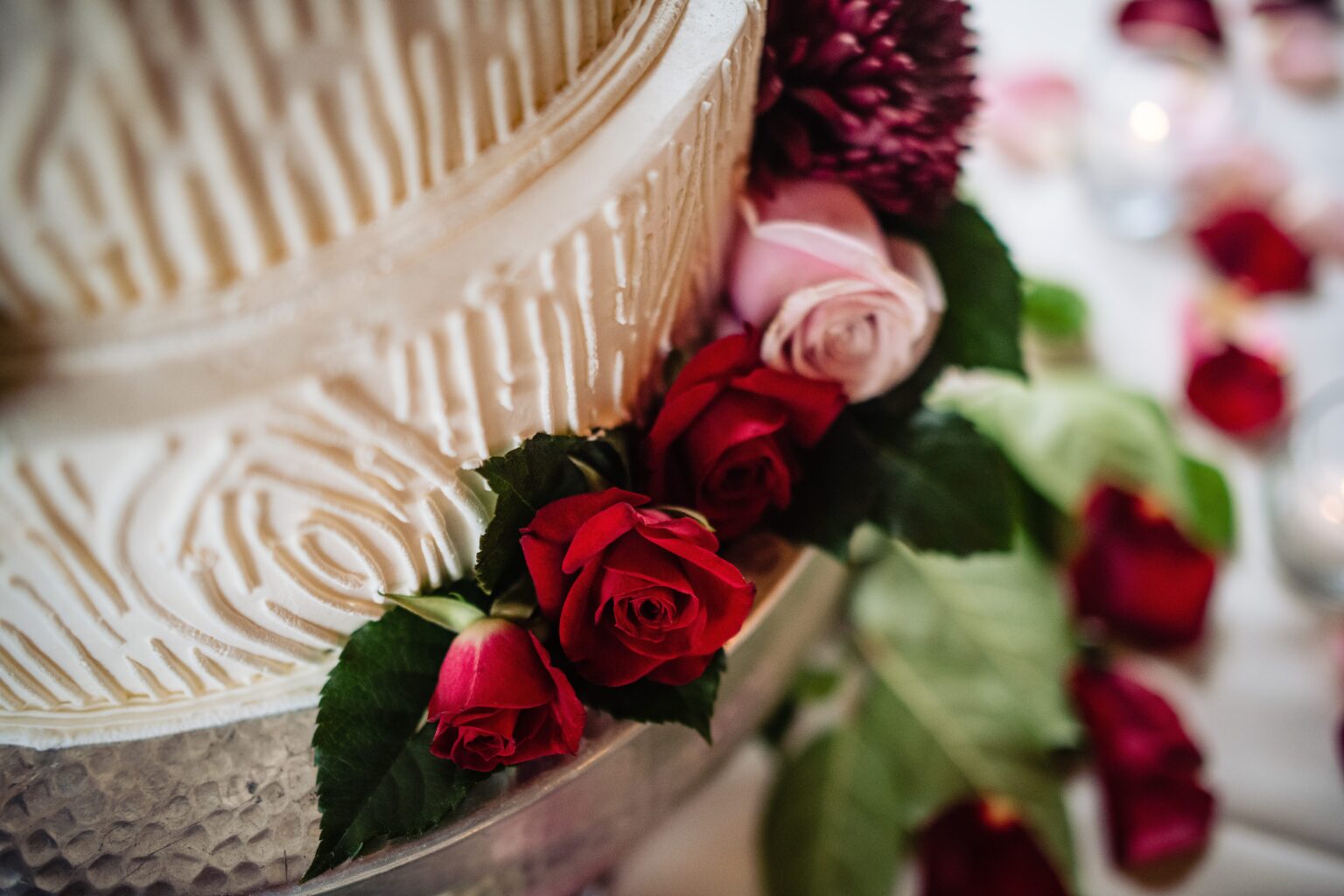 Red and pink roses adorn white wedding cake