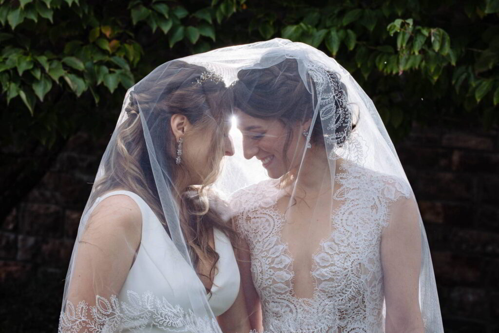 Two brides touch foreheads beneath bridal veil