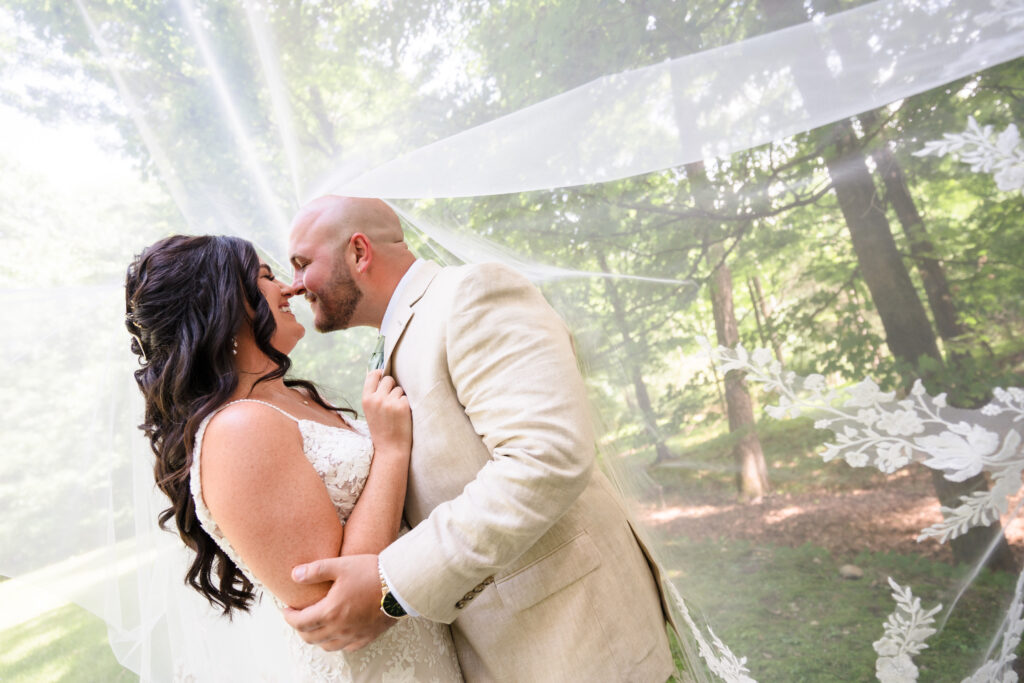 Bride and groom touch noses beneath bridal veil