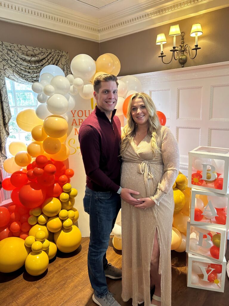 Couple poses together in front of balloon arch