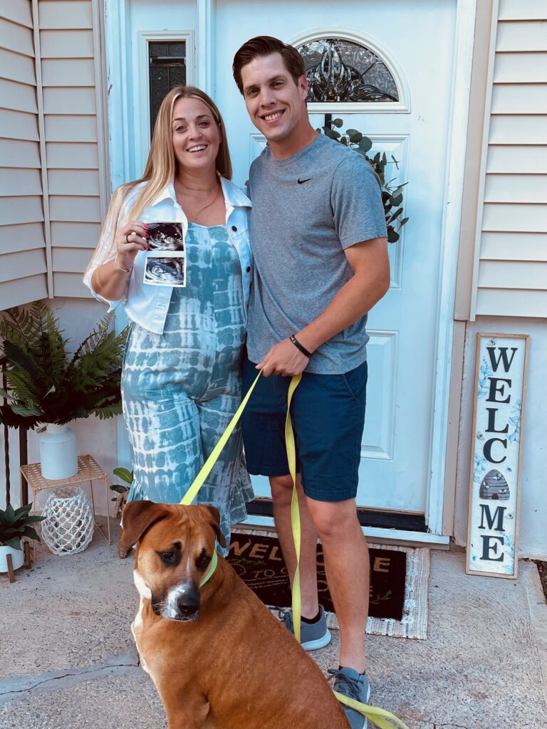 Couple smiles outside their new home with their puppy