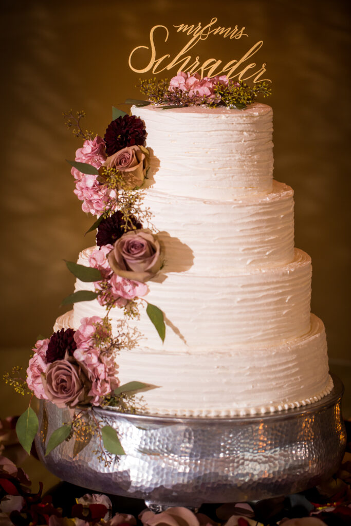 Four-tier wedding cake with topper and pink and purple flowers