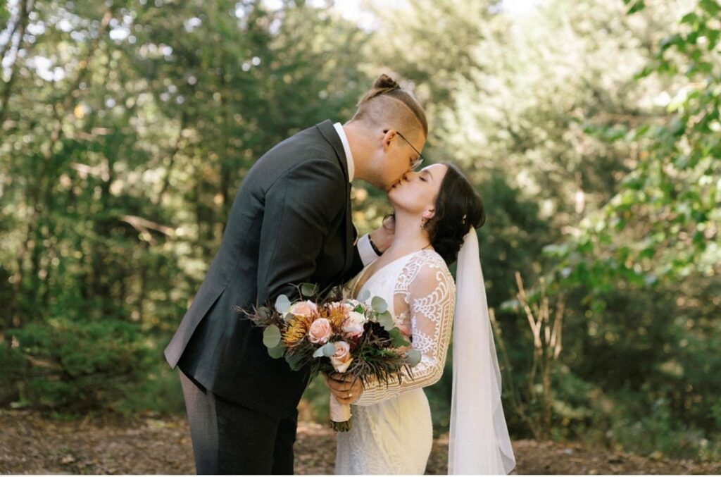 Bride and groom kiss beneath tree canopy